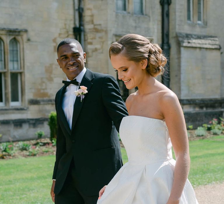 Groom in black tie wearing a colourful buttonhole walks with the bride in a Jesus Peiro brocade wedding dress 