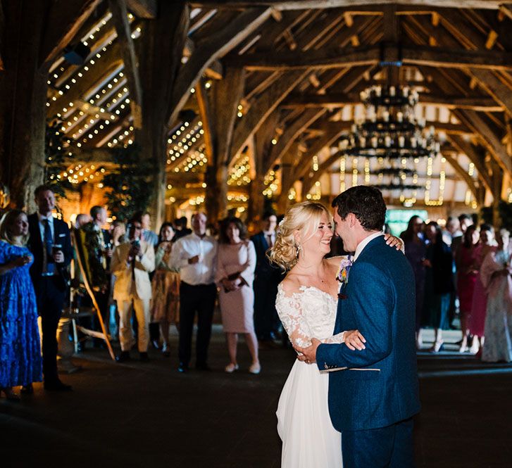 Bride & groom have their first dance as wedding guests watch on and fairy lights hang from the ceiling 