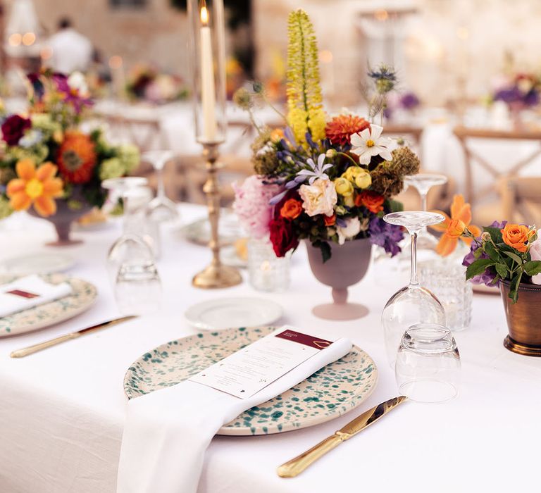 Speckled white and green plates with small colourful flower arrangement and gold cutlery