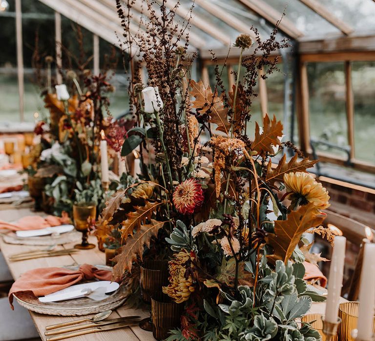 Orange and red warm toned wedding flower centrepieces with coloured glassware for the mini pumpkin decor