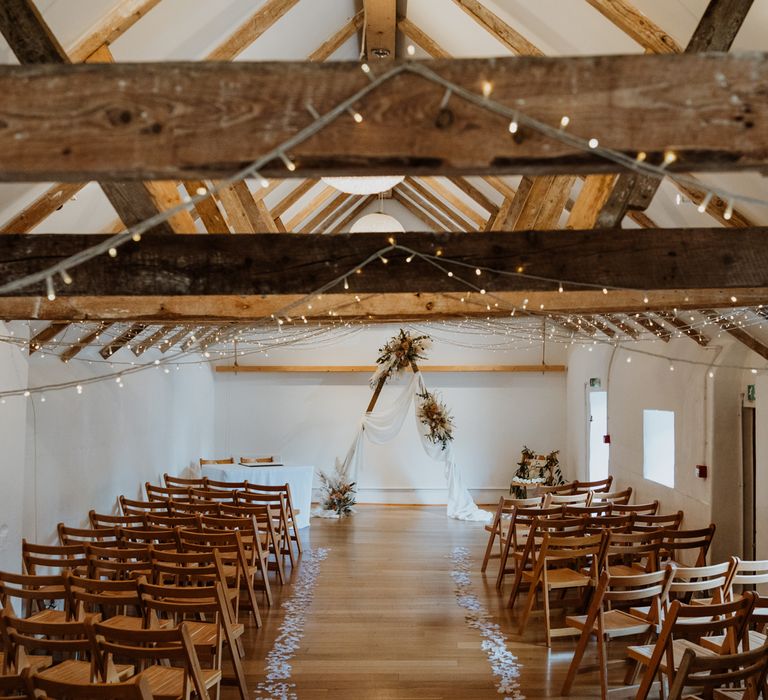 The Green Cornwall wedding venue reception room with fairy lights interwoven in the large wooden beams and a triangular wooden arch with dried flower arrangements