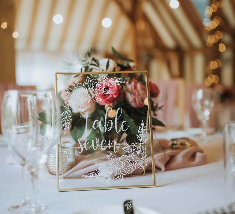 Gold photo frame table name on a white tablecloth with pink flower centrepiece