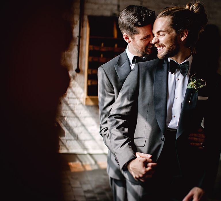 Grooms embrace whilst wearing black-tie suits complete with botanical buttonholes 