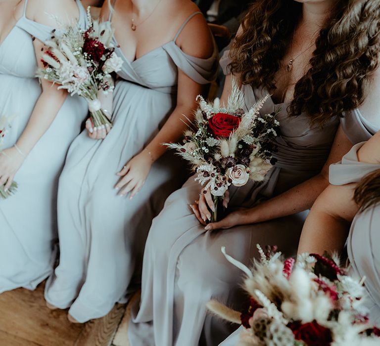 Bridesmaids in light grey bridesmaid dresses holding red rose, white flower and bunny grass bouquets