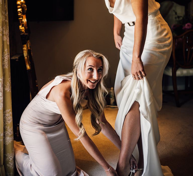 Bridesmaid helps bride with her shoes on the morning of her wedding day