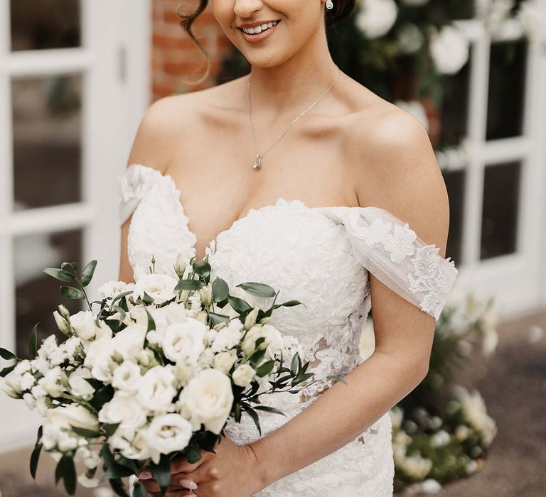 Bride in a flower lace wedding dress with a white bouquet and hair in an updo complete with silver jewellery