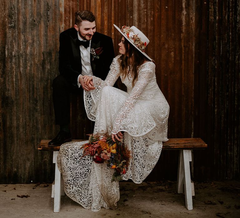 The bride and groom sit together on a wooden bench for their couple portraits at the rustic Silchester Farm 