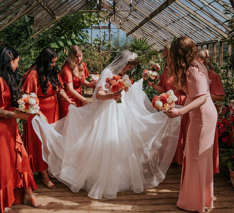 The bridesmaids in coral peach bridesmaid dresses all fuss over the bride in her tulle wedding dress 