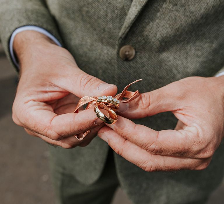 Groom holding the gold wedding bands for the bride and groom tied together with ribbon