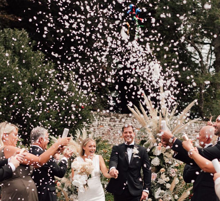 Bride and groom walk back down the aisle as white confetti explodes over them at their outdoor ceremony 