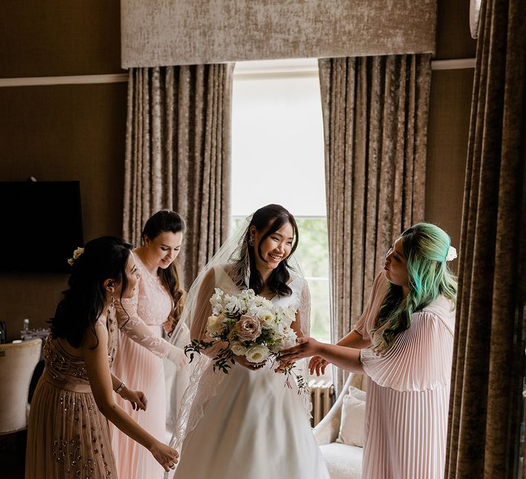 Bride wears Princess wedding dress and is surrounded by her bridesmaids in pastel pink dresses 