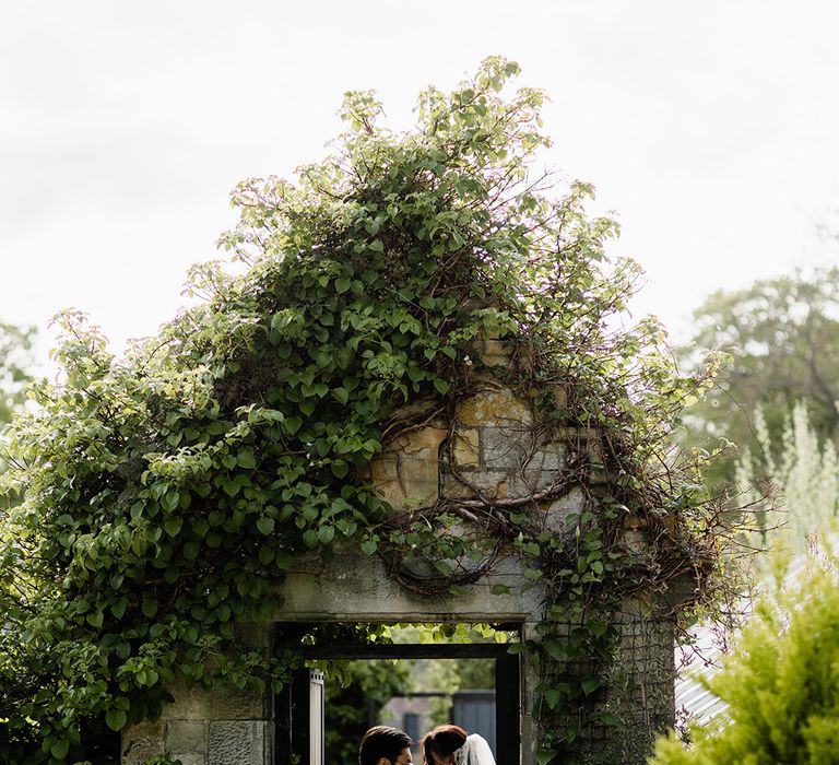 Bride & groom stand within rustic doorway outdoors at Carlowrie Castle before Chinese Tea Ceremony