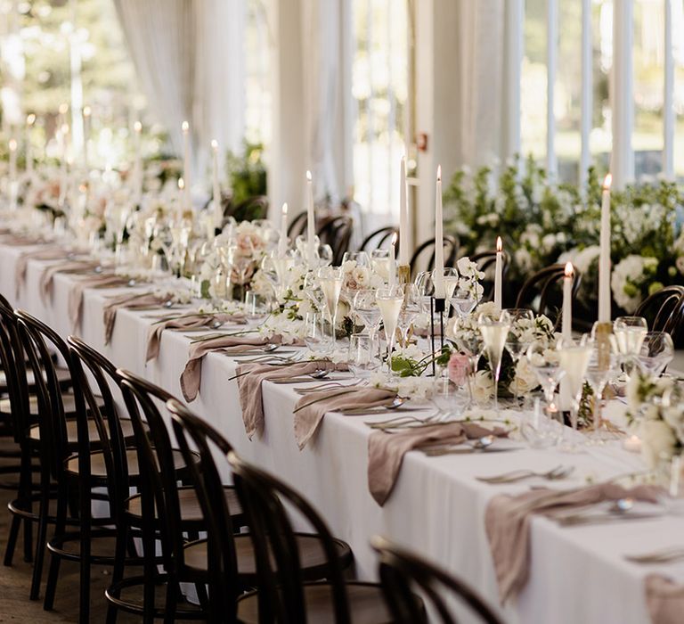 Small floral arrangements line banquet table covered with white tablecloth and fabric pink napkins 