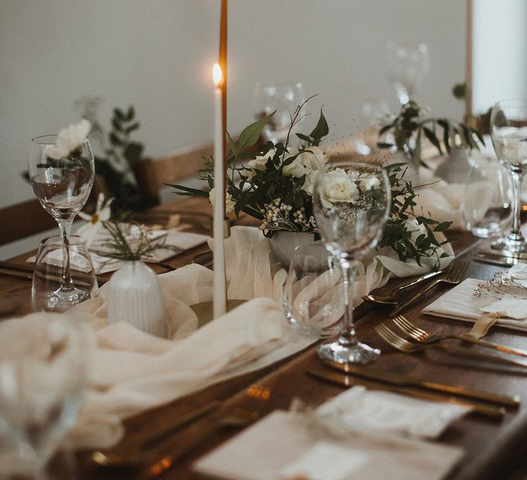 Classic tablescape complete with white fabric table runner, small white floral arrangements and white candles 