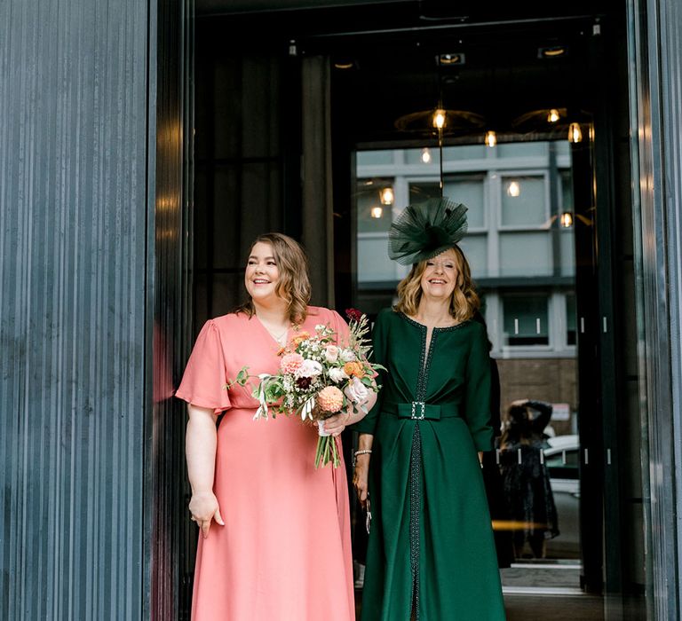 Bridesmaid wears pink batwing Rewritten Bridesmaid dresses whilst stood beside Mother Of The Bride in deep green dress