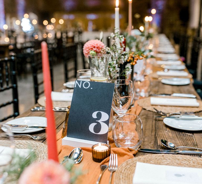 Wooden banquet tables complete with orange fabric table runners and pastel coloured candles in black candle holders 