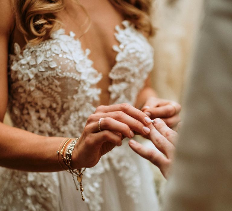 Bride in white embroidered low cut wedding dress exchanging rings with groom