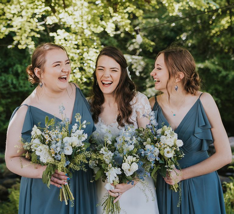 Bridesmaids in matching blue ruffle bridesmaid dresses with the bride in beaded wedding dress holding white and blue bouquets 