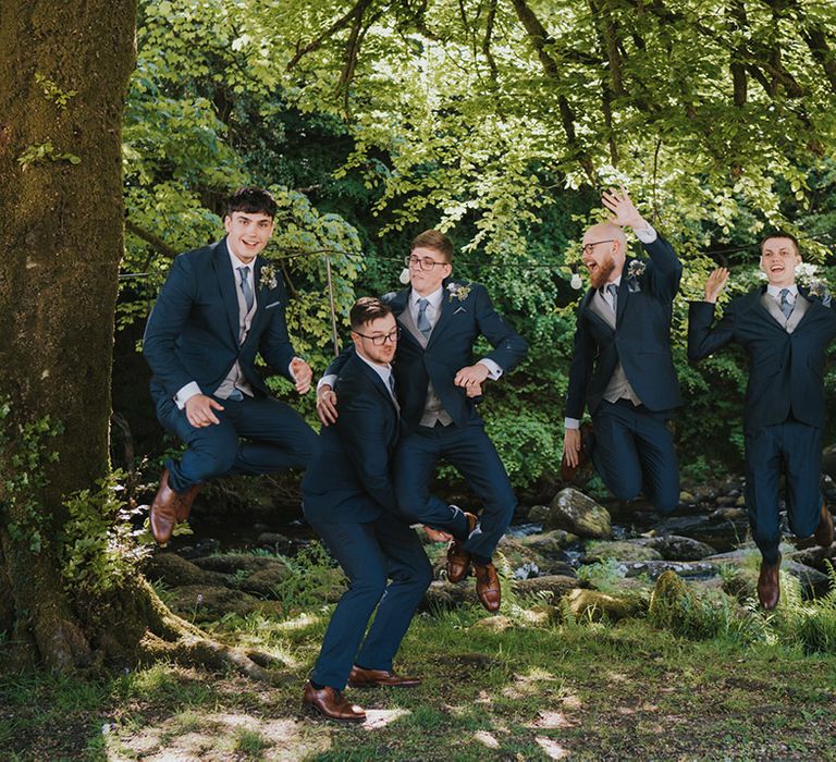 Groomsmen all jump in the air for fun wedding photo in navy wedding suits for blue theme wedding