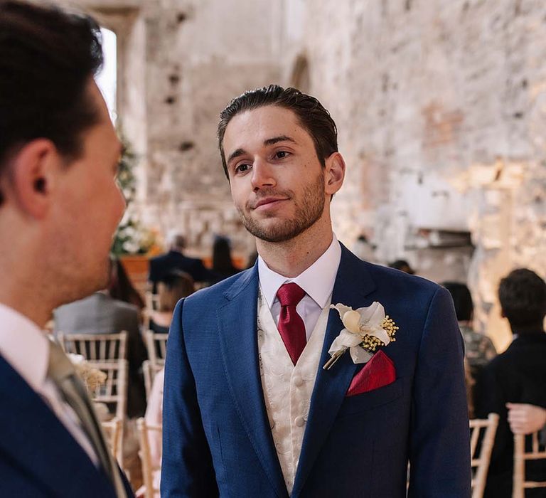 Groom in bright blue wedding suit with white waistcoat and red tie for the luxury wedding day 