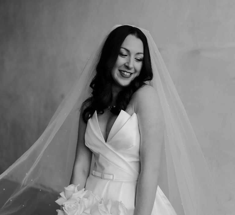 Bride in silk wedding dress with a sweetheart neckline and wedding veil holding white rose bridal bouquet 