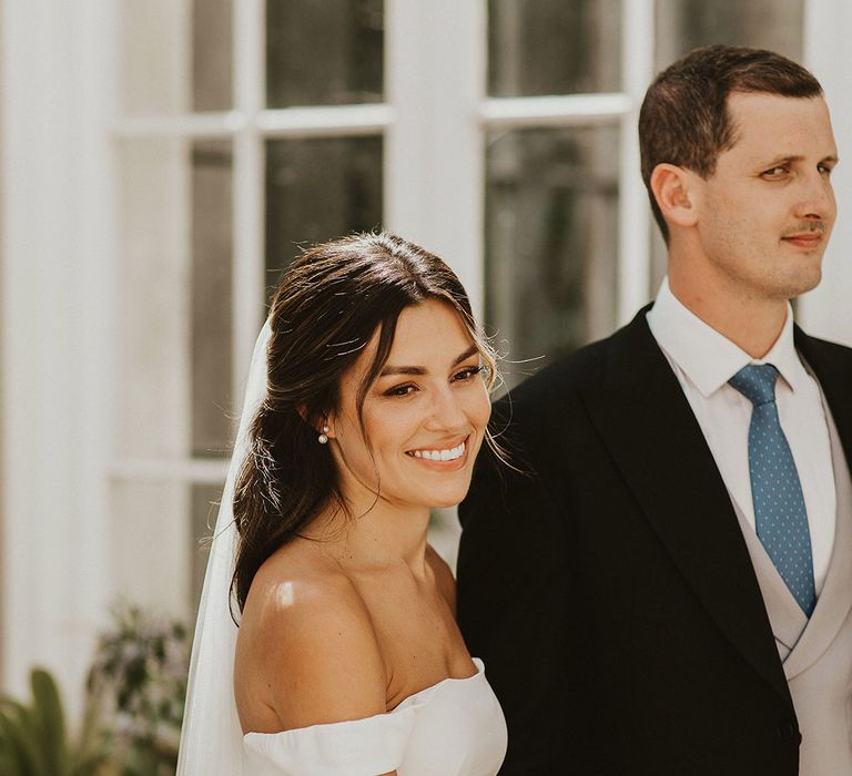 Groom in traditional morning suit with white rose buttonhole walking holding hands with the bride in an off the shoulder minimalist dress with white flower bouquet | Steph Newton Photography