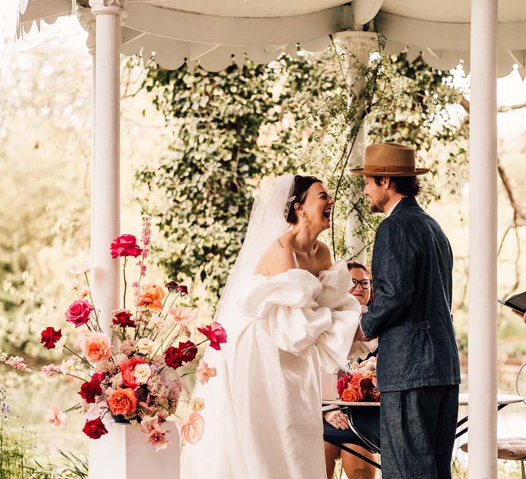 The bride and groom hold hands under the gazebo at Preston Court for their outdoor ceremony 