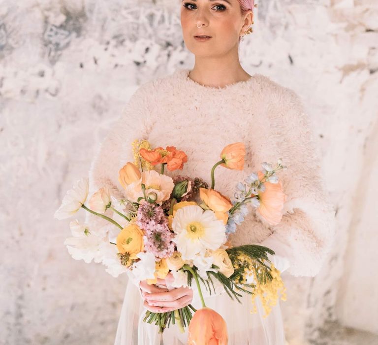 Bride in sheer overlay wedding dress and fluffy bridal coverup holding orange bridal bouquet in Margate Caves 