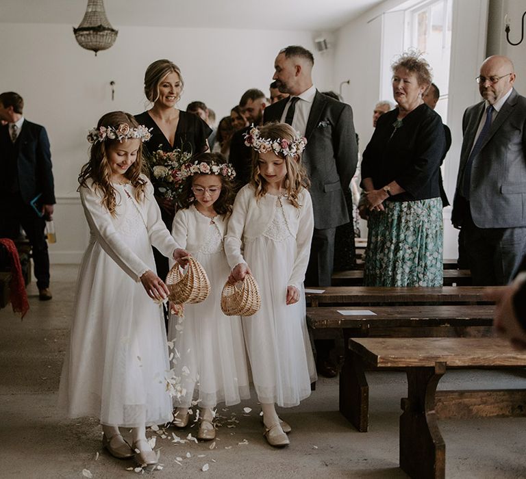 Flower girls in pretty white flower girl dresses with flower crowns throwing white petals down the aisle 