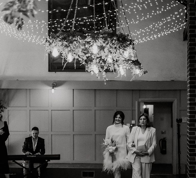 Bride walks down the aisle with the mother of the bride in white suit 