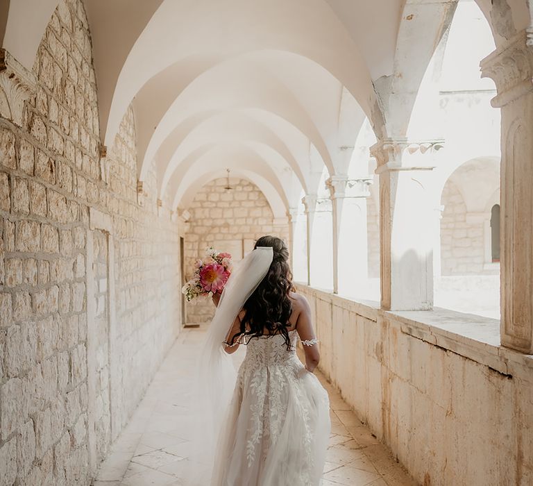 Bride in 3D lace wedding dress walks through historic monastery at wedding ceremony in Hvar, Croatia