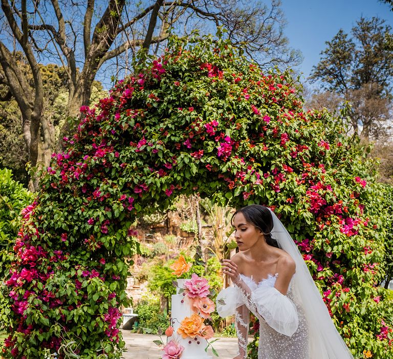 Bride in wedding dress with detachable sleeves cut the white wedding cake 