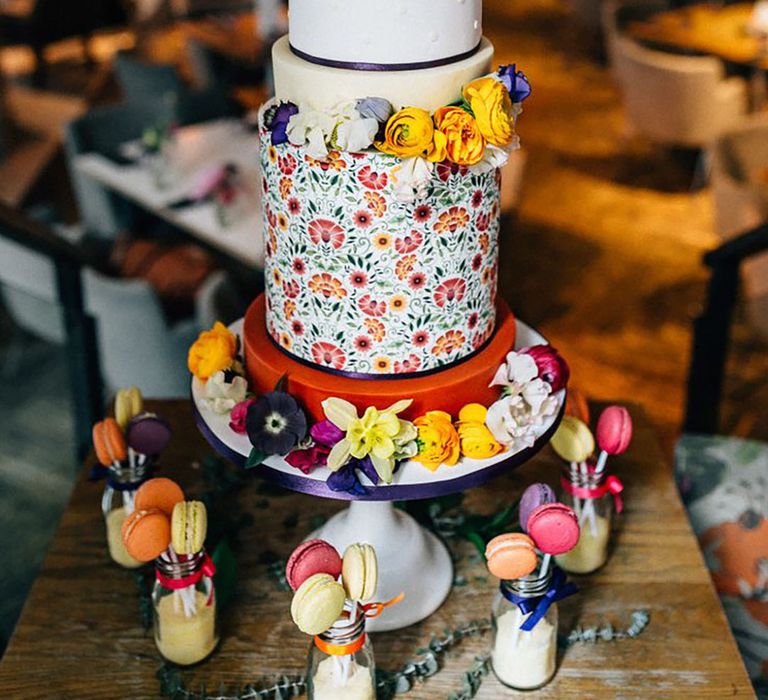 Five tier wedding cake topped with bright colourful peonies and wedding flowers with every tier decorated in different colours or patterns 