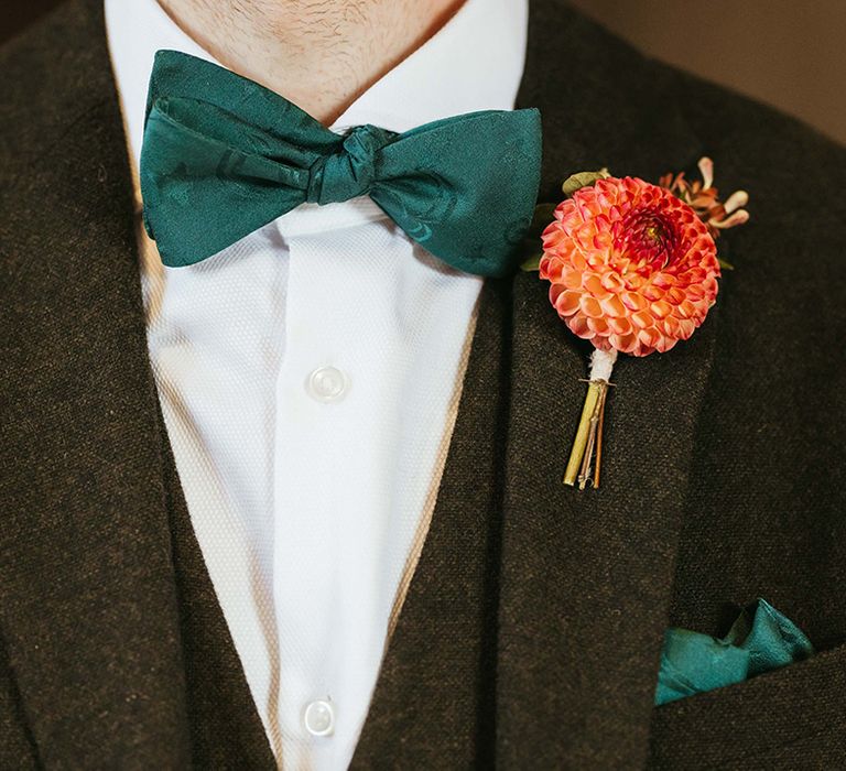 Dahlia flower buttonhole accessory for the groom in a black suit with green bow tie and pocket square 