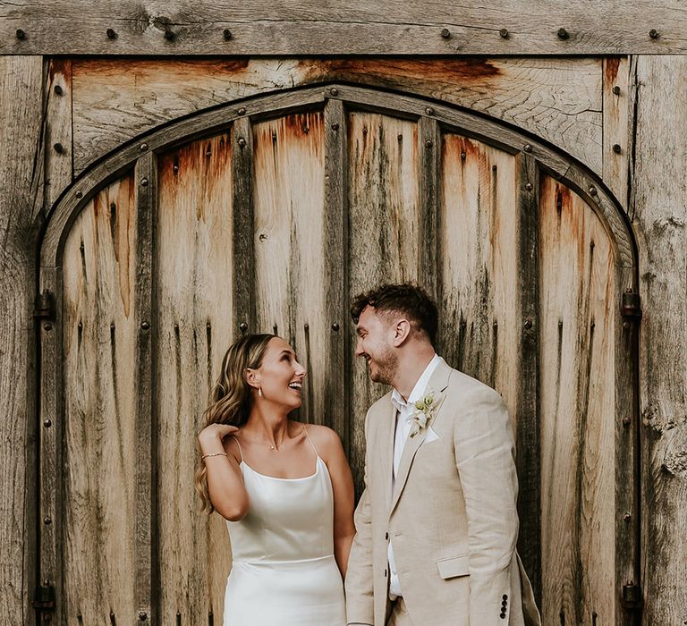 Bride in simple satin minimalist wedding dress with groom in beige suit at Shustoke Barns wedding in Warwickshire 