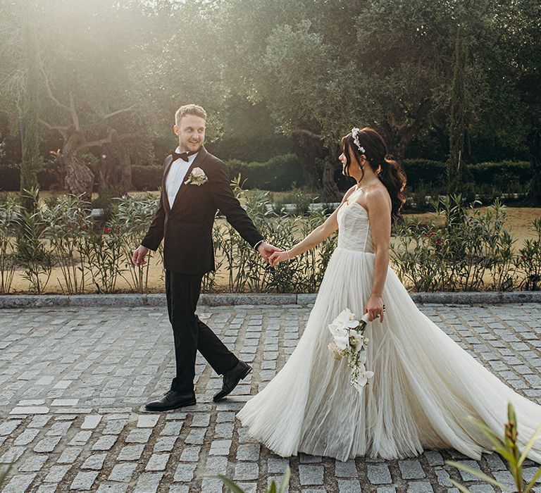 Bride wearing princess wedding dress walking with the groom in a black tux carrying neutral wedding bouquets 