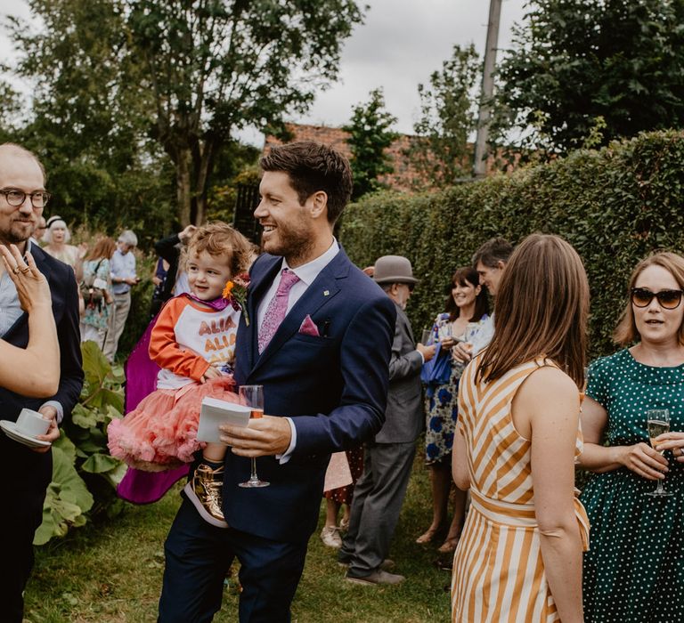 Groom in navy suits holding his daughter in pink tutu 