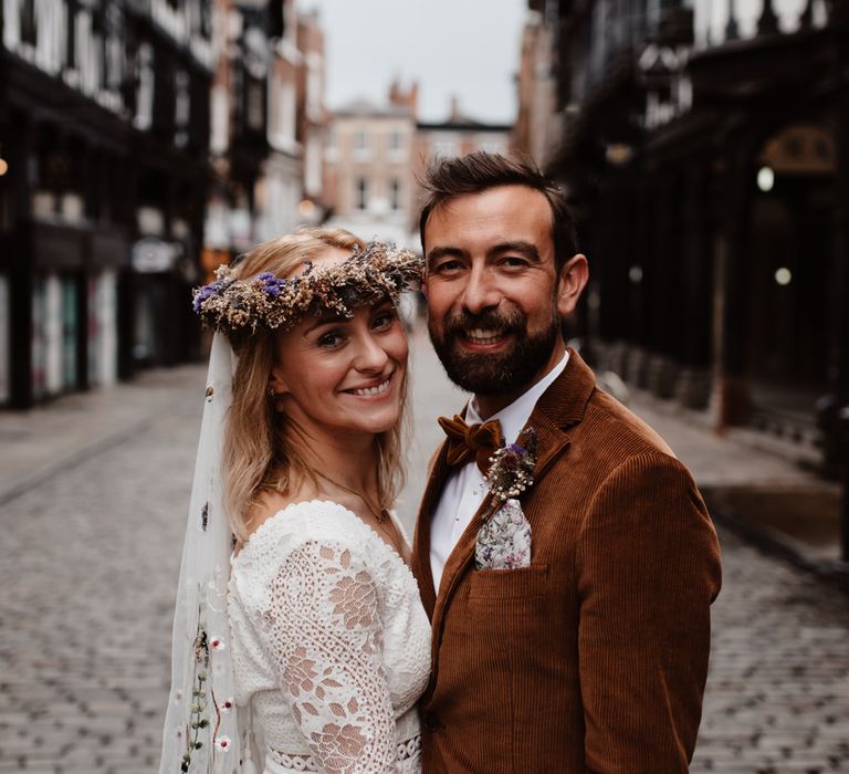 Boho bride in lace dress, embroidered veil and flower crown and groom in cord jacket 