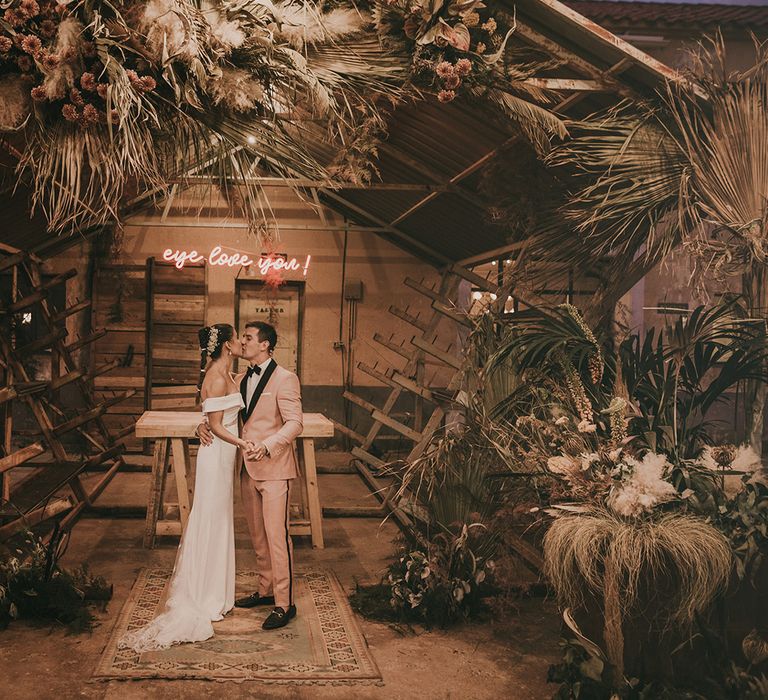 Bride and groom kissing under a pink neon sign 