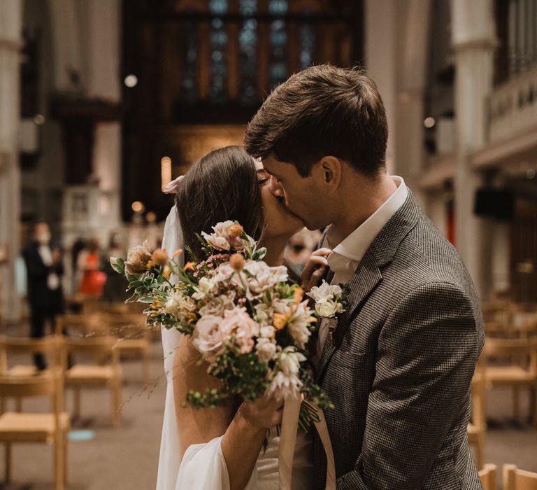 Groom in check jacket kissing his bride in a slip wedding dress