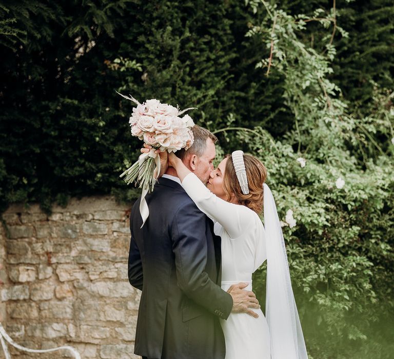 Bride in Elbeth Gillis gown and beaded bridal headband kisses groom whilst holding blush pink rose bouquet at Euridge Manor wedding