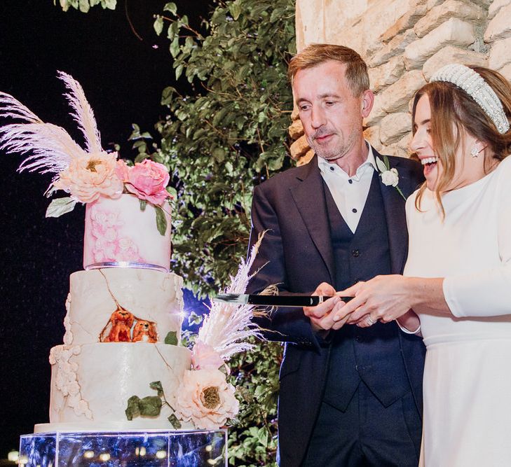 Smiling bride in Elbeth Gillis gown and groom in navy Cad & the Dandy suit cut three tier wedding cake at Euridge Manor wedding