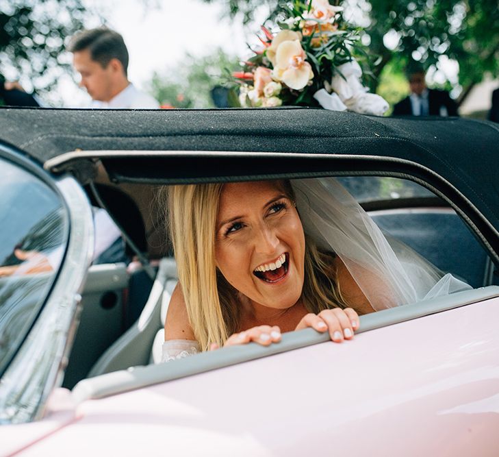 Bride sat in pink Porsche smiling through the window on her wedding day