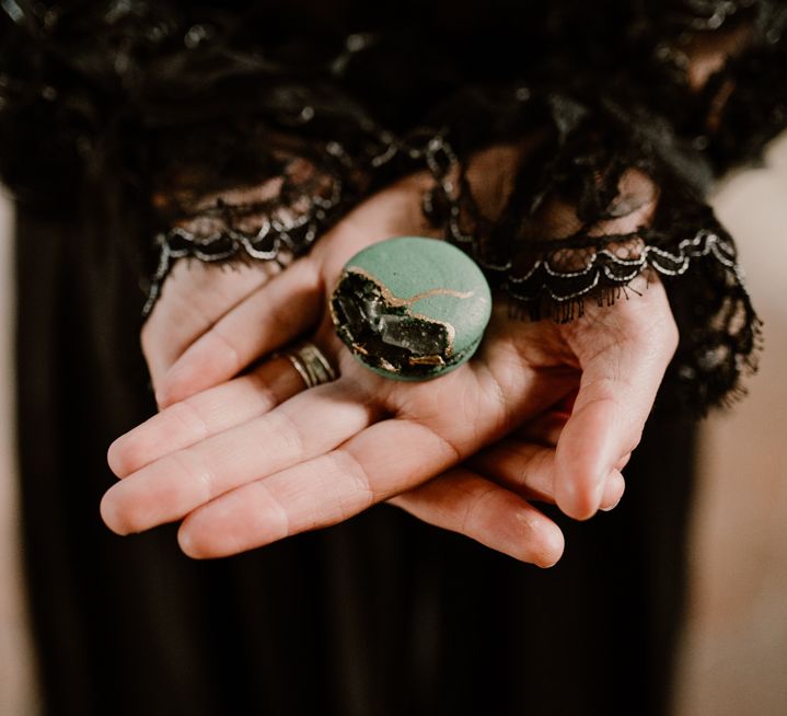 Bride in a long sleeve black lace wedding dress holding a green macaroon 