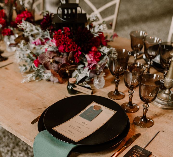 Place setting with black table and glassware, green linen and red wedding flowers 