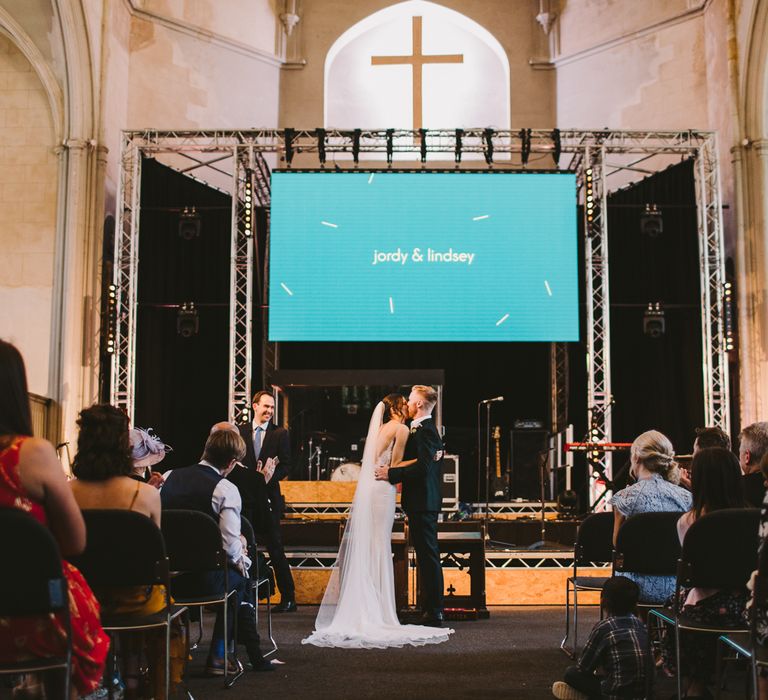 Bride & groom during wedding ceremony with screen in the background with their name