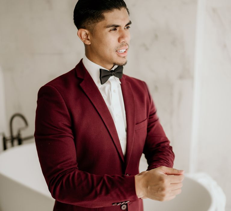 Groom in a dark red tuxedo jacket with bow tie on the wedding morning