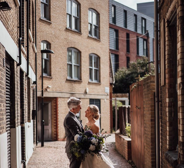 Bride & groom stand in cobbled street of London 