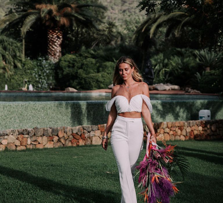 A blonde bride wears bridal separates. The cropped top has a bardot neckline and she wears trousers. Photography by Stephanie Shenton.