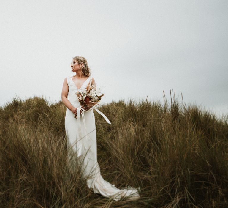 Bride walks through grass verge to get to beach for first look moment